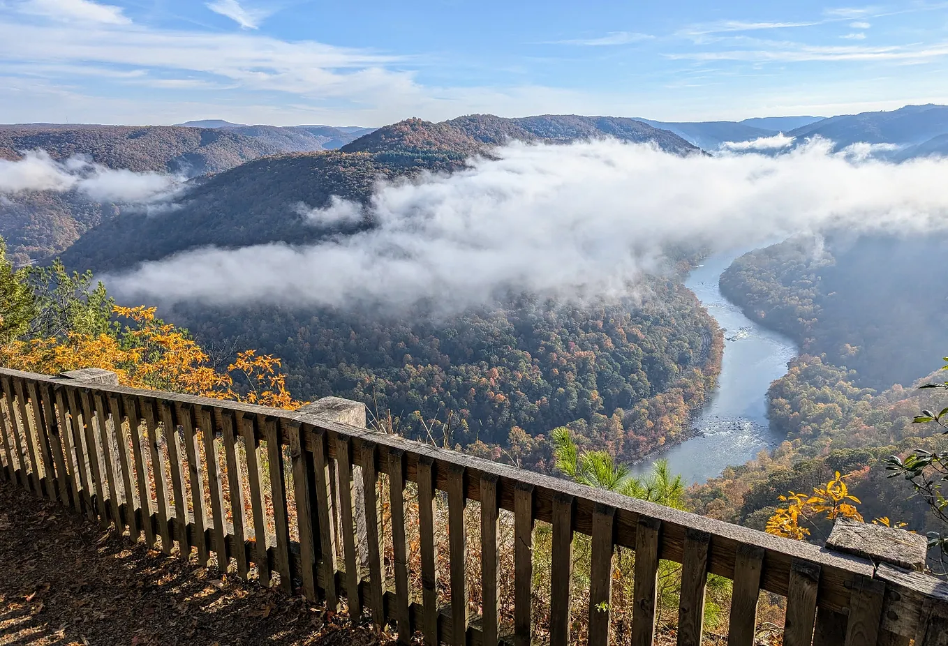 A wide-angle view of the New River Gorge with morning mist partially obscuring the river and mountains.