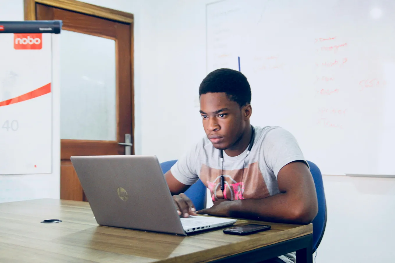 Young man sits a desk looking at a laptop.