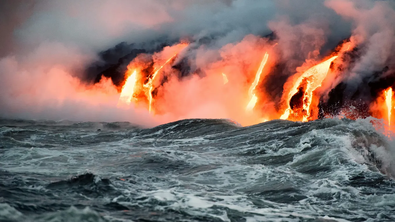 The image shows a dramatic scene of molten lava pouring into the ocean, creating plumes of steam as the intense heat meets the turbulent waves. The bright orange glow of the lava contrasts with the dark, stormy waters, highlighting the powerful interaction between volcanic activity and the sea.