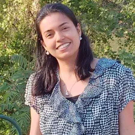 Image of Bhavana Dalvi, a woman with shoulder-length brown hair wearing a black and white blouse standing in front of some trees.