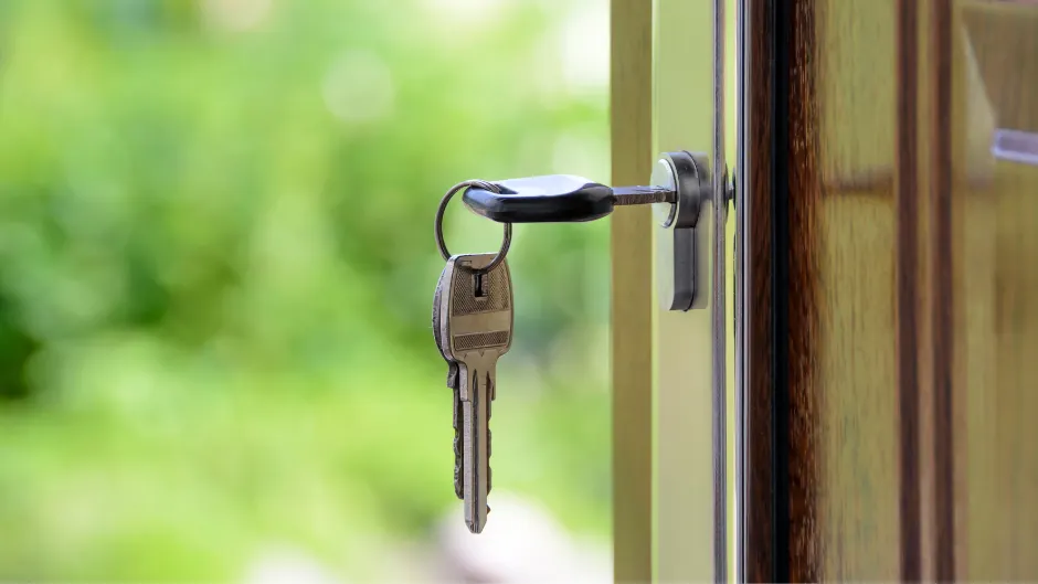 Key in front door key hole, blurred greenery in background as front yard