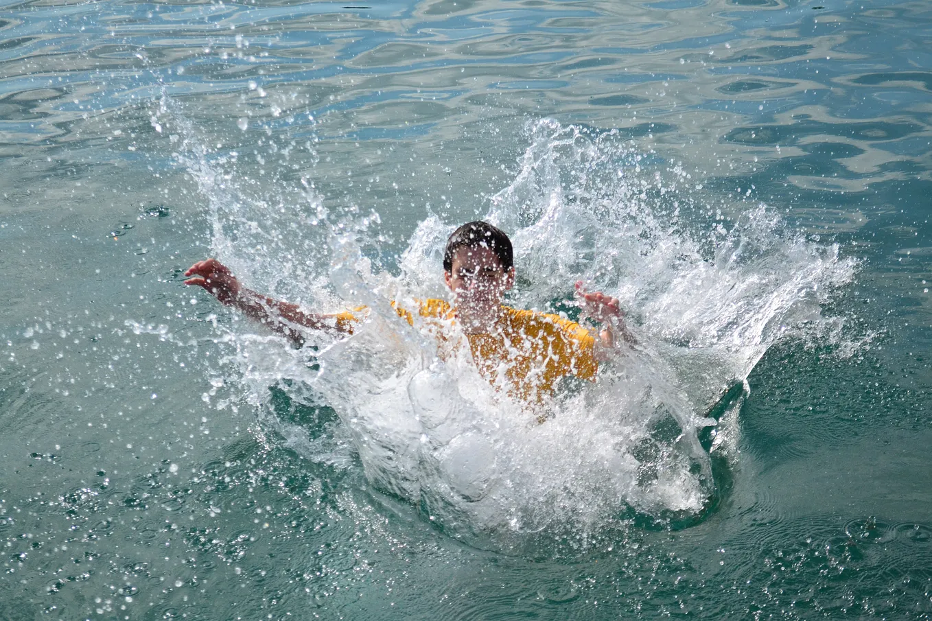 A person wearing a yellow shirt is splashing in the water.