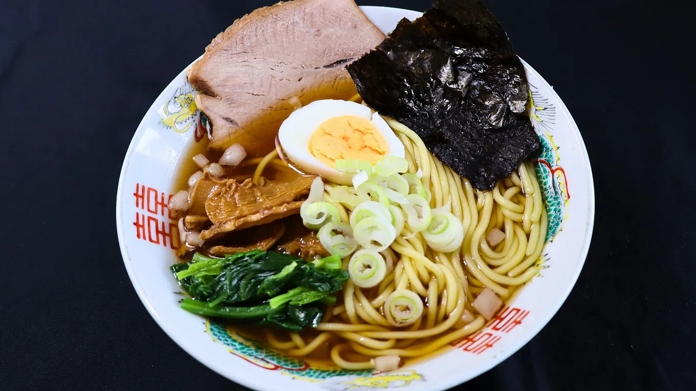 A bowl of shoyu ramen topped with sliced pork, a boiled egg, green onions, spinach, menma, and a sheet of nori.