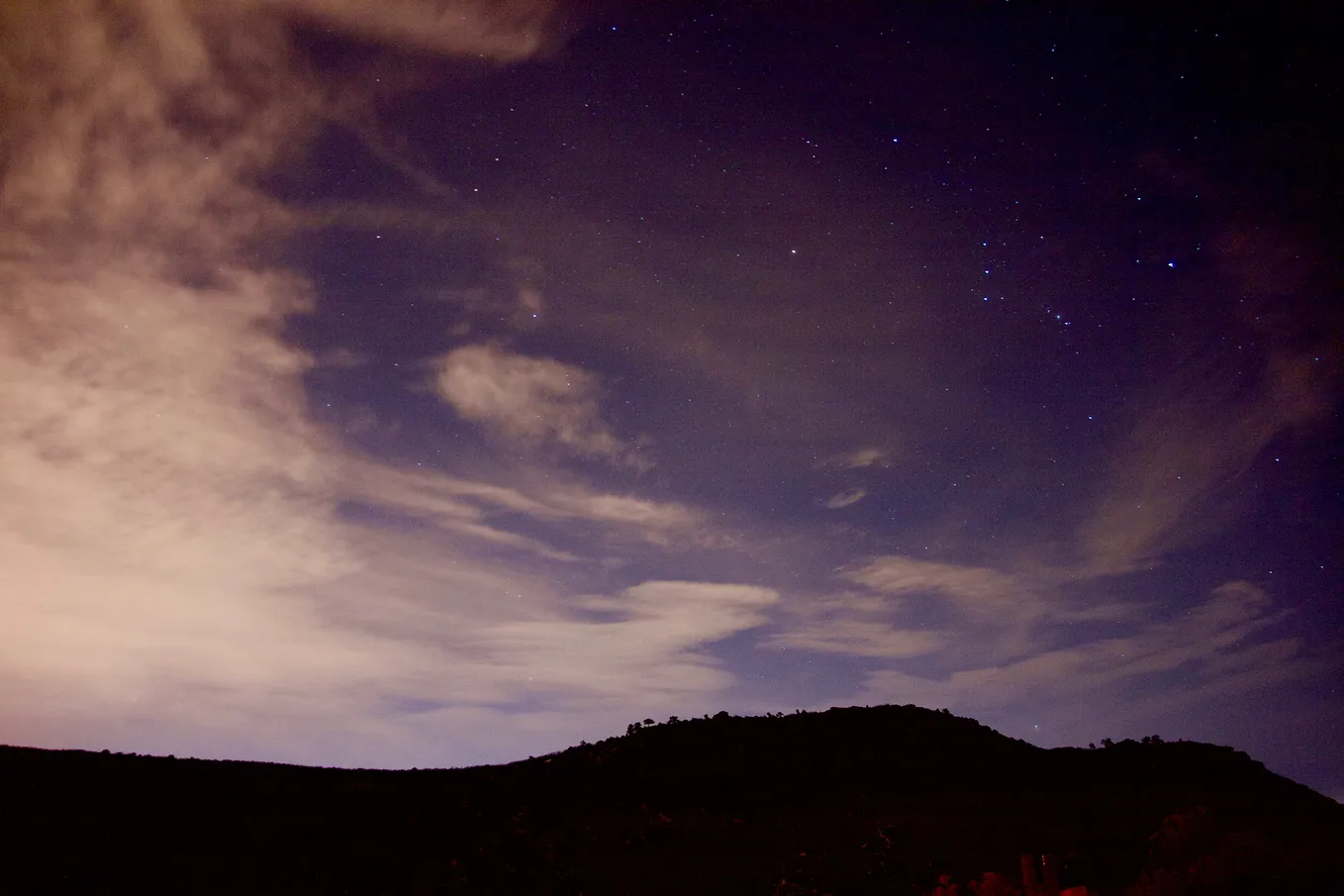 A night landscape of a night sky with some stars visibe behind whispy clouds.
