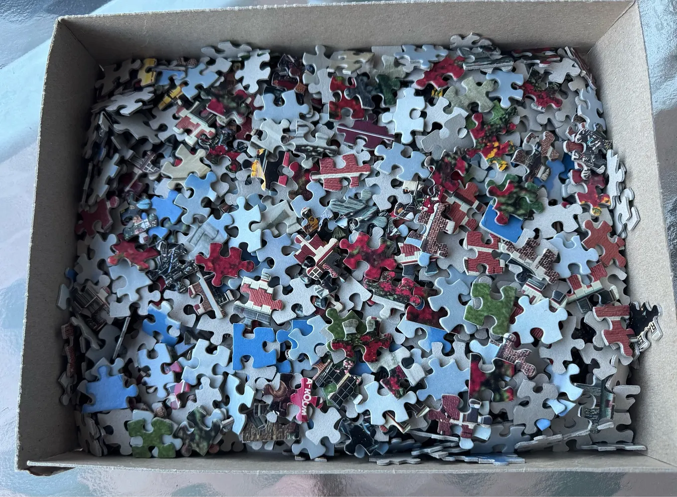 A shallow cardboard box hold thrpieces of a jigsaw puzzle