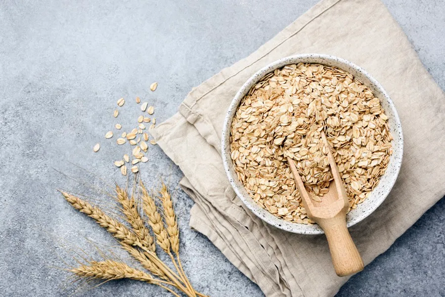 A bowl of traditional rolled oats sitting on a linen towel with a wooden scoop