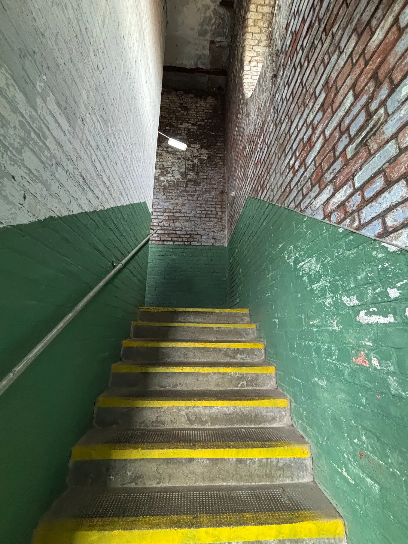 Looking up a concrete staircase, with brick walls partly painted green.