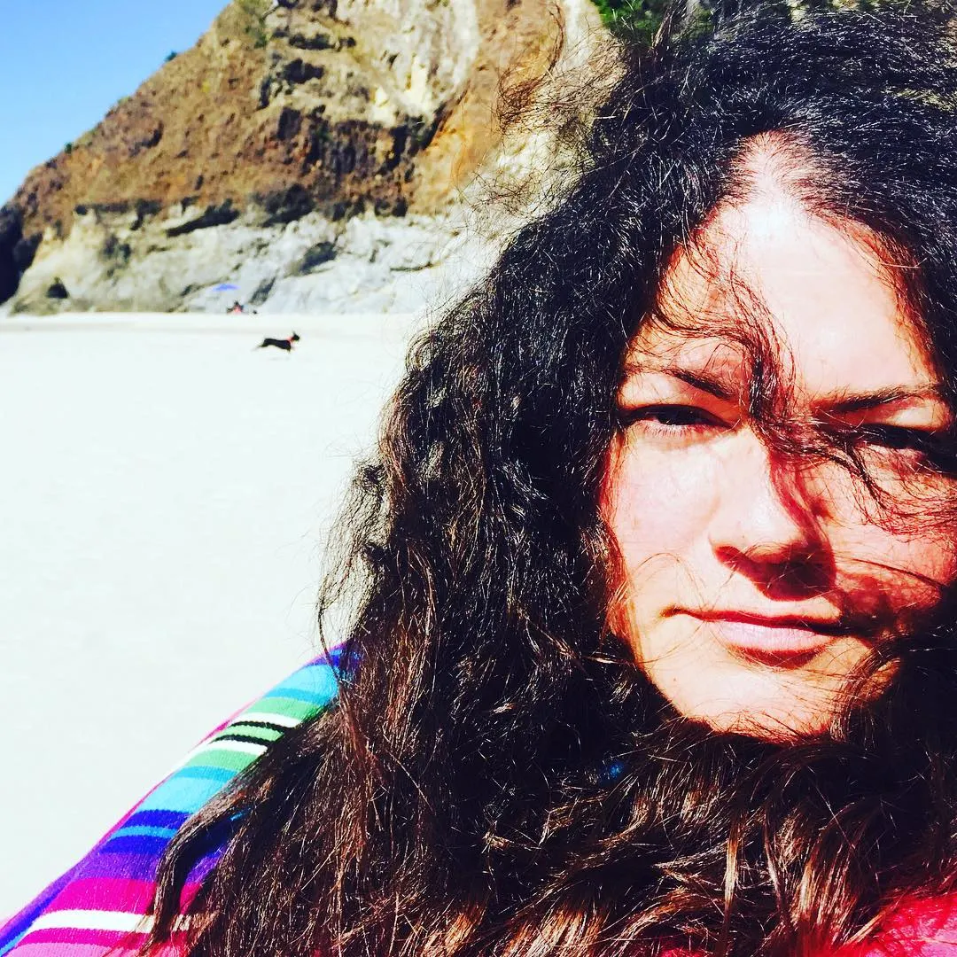 Closeup of a woman with curly hair sits on a sunny beach
