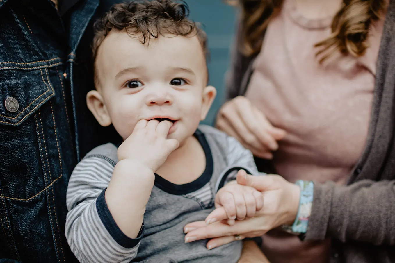 A toddler with his hand in his mouth, holding a woman’s hand. A Grain of Infinfity