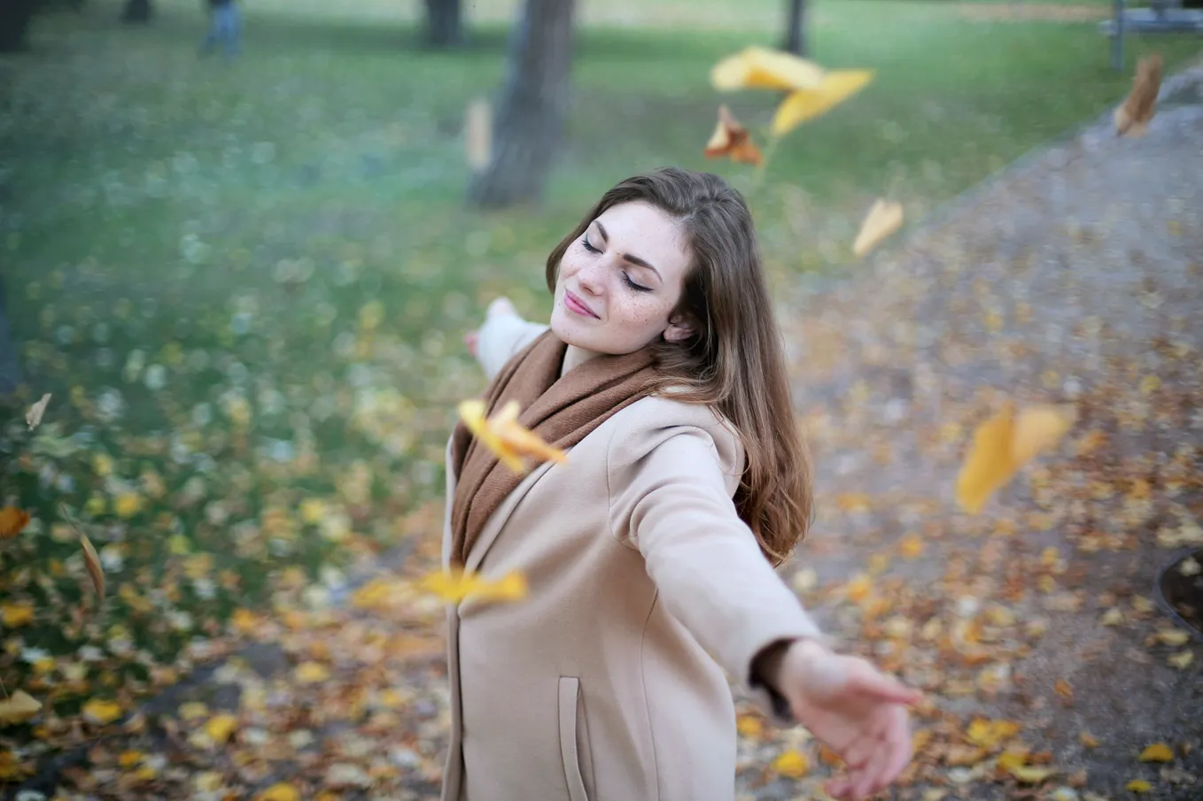 A woman enjoying the spring season where the dry leaves are flying around her.