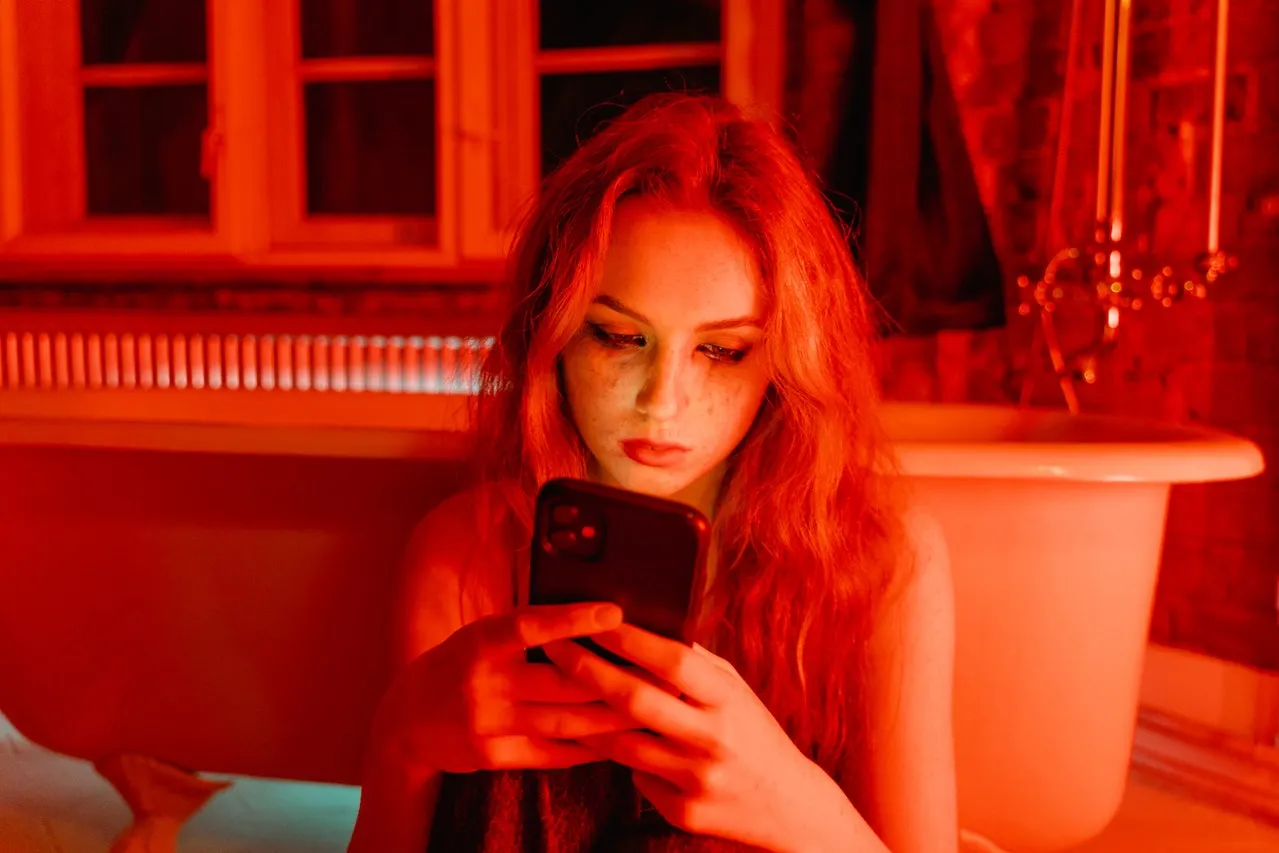 A sad woman with streaked mascara holds a phone in her hands