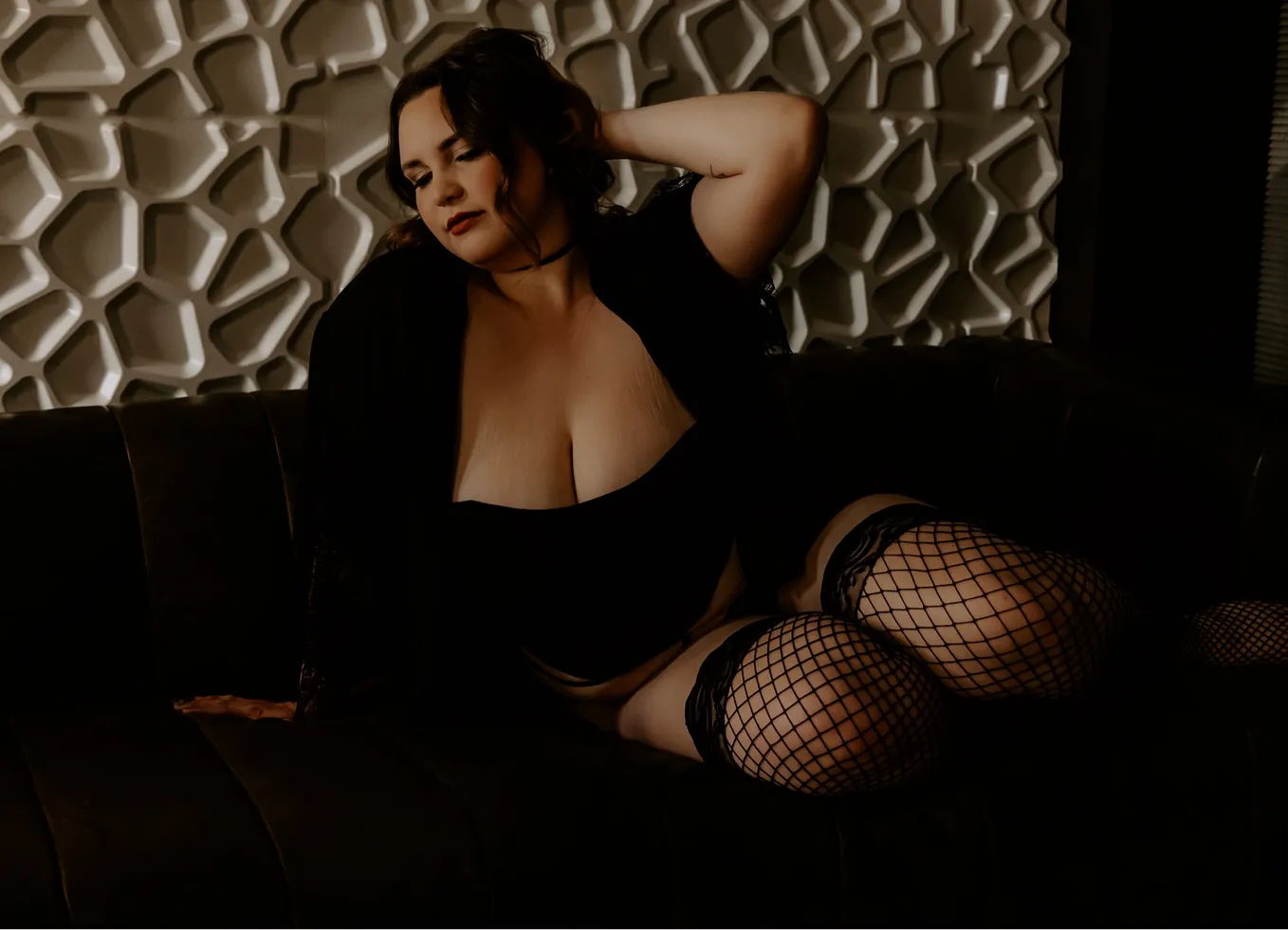 Liz poses on a couch in black lingerie and fishnets.