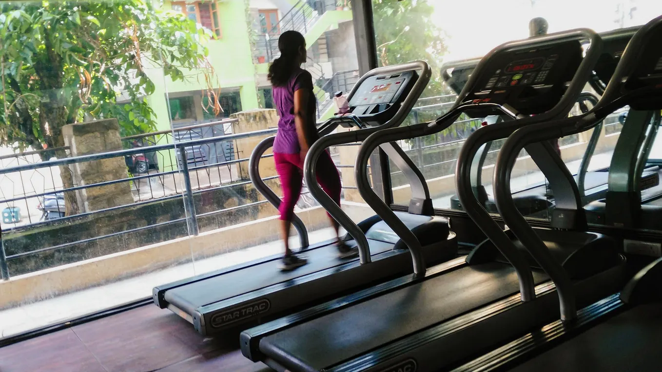 Woman on a treadmill at a gym looking outside through the glass walls