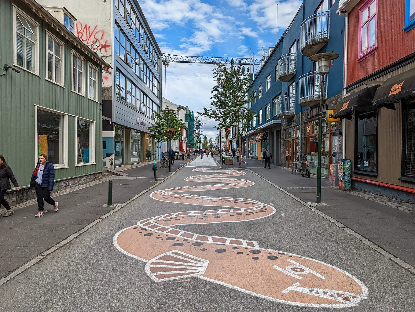 A straight city street going up a hill, with a painting of a twisting eel down the middle of the street