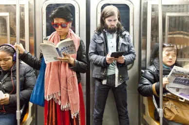 People on the subway, one on their phone, one reading a book.