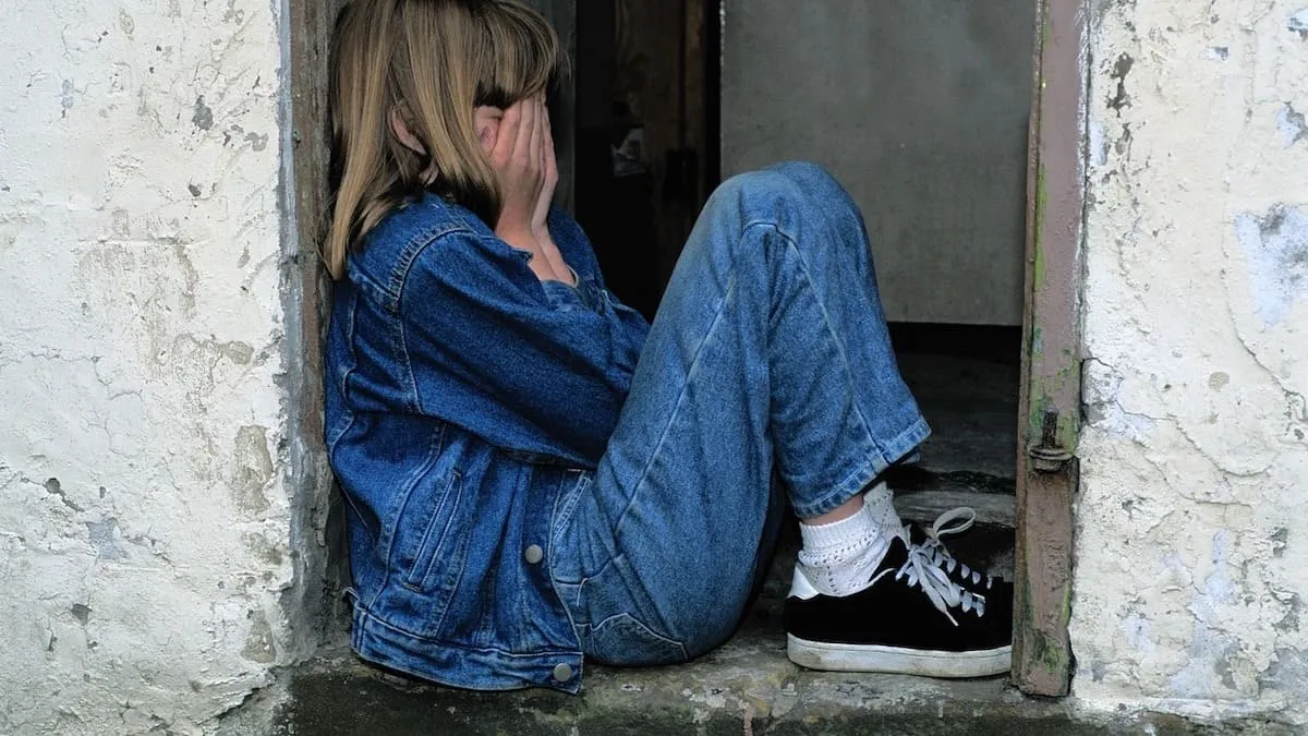 child sitting in a doorway, hands covering face