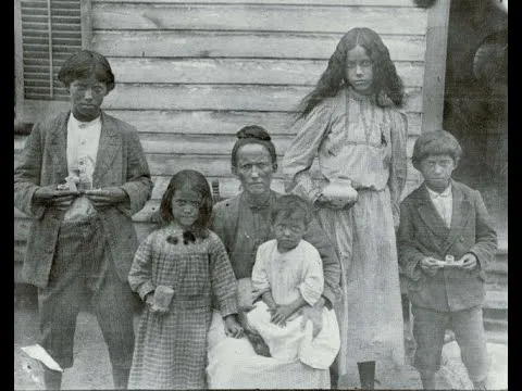 Black and white photo depicting a dark skinned woman with black hair pulled into a bun, surrounded by her 5 children.