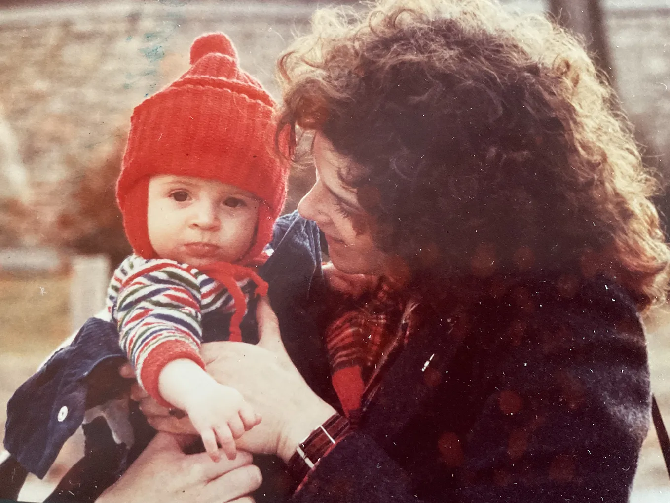 A curly headed mother holds her 8 month old red winter capped baby.