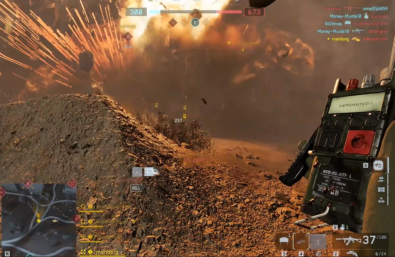 First-person view in Battlefield 6 showing a player triggering a remote detonator as a massive explosion erupts ahead, sending debris and fire into the air across a dusty battlefield. The HUD displays team scores, objectives, a minimap, and ammo count during the chaotic moment.