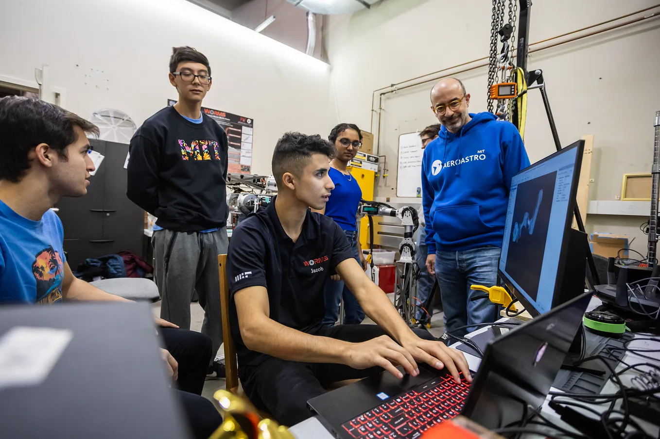 A learner types on a computer as four people watch. One of the people is wearing a black sweatshirt that says MIT.