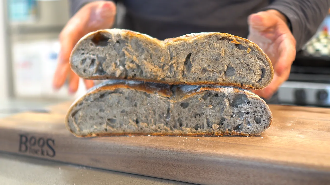 A sourdough loaf with one half on top of the other and the bakers’ hands behind it.