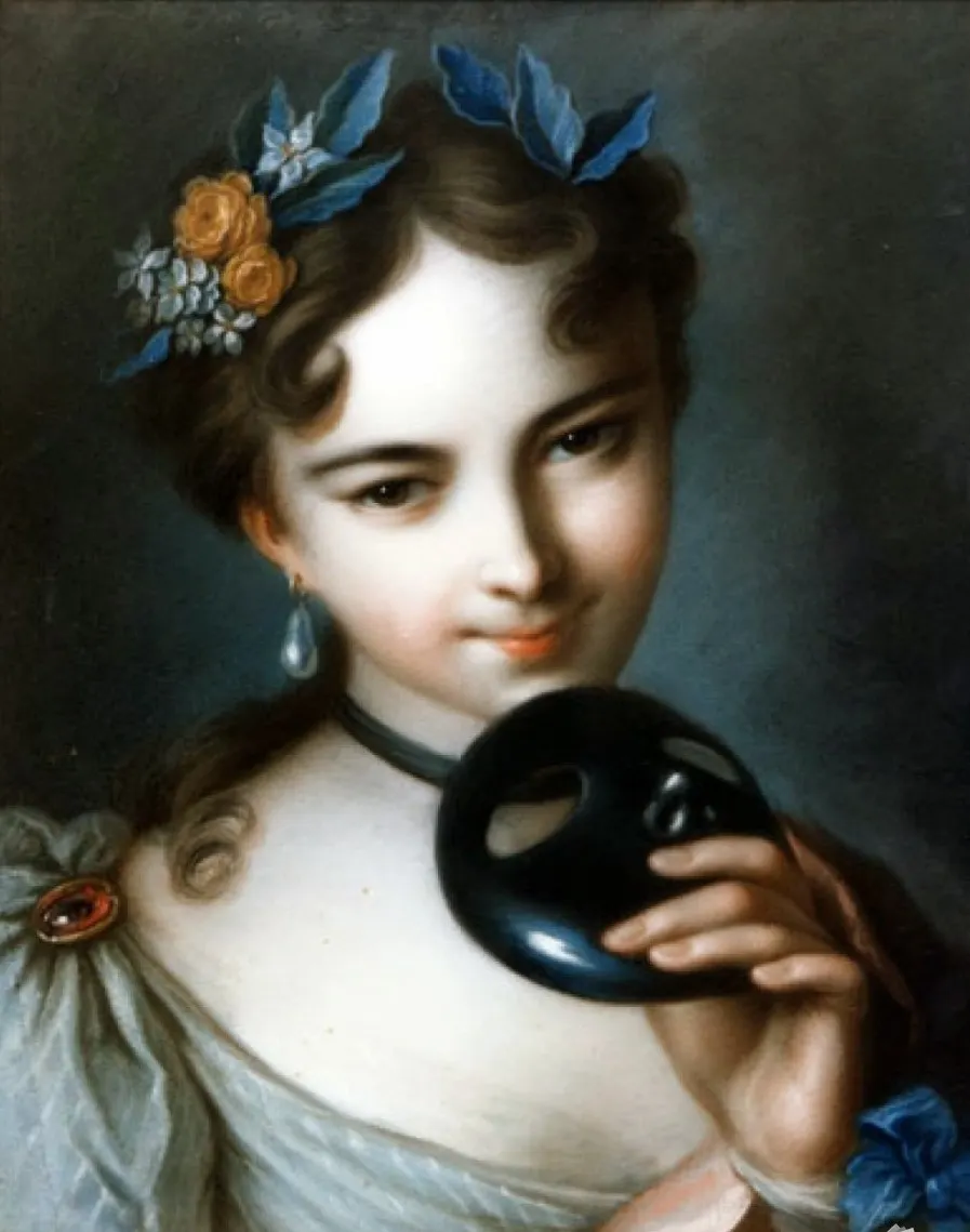 Color portrait of a smiling young woman with dark hair and eyes, wearing large pearl earrings and flowers in her hair. She holds a small black face mask in her hand, partially hiding her chin and neck.