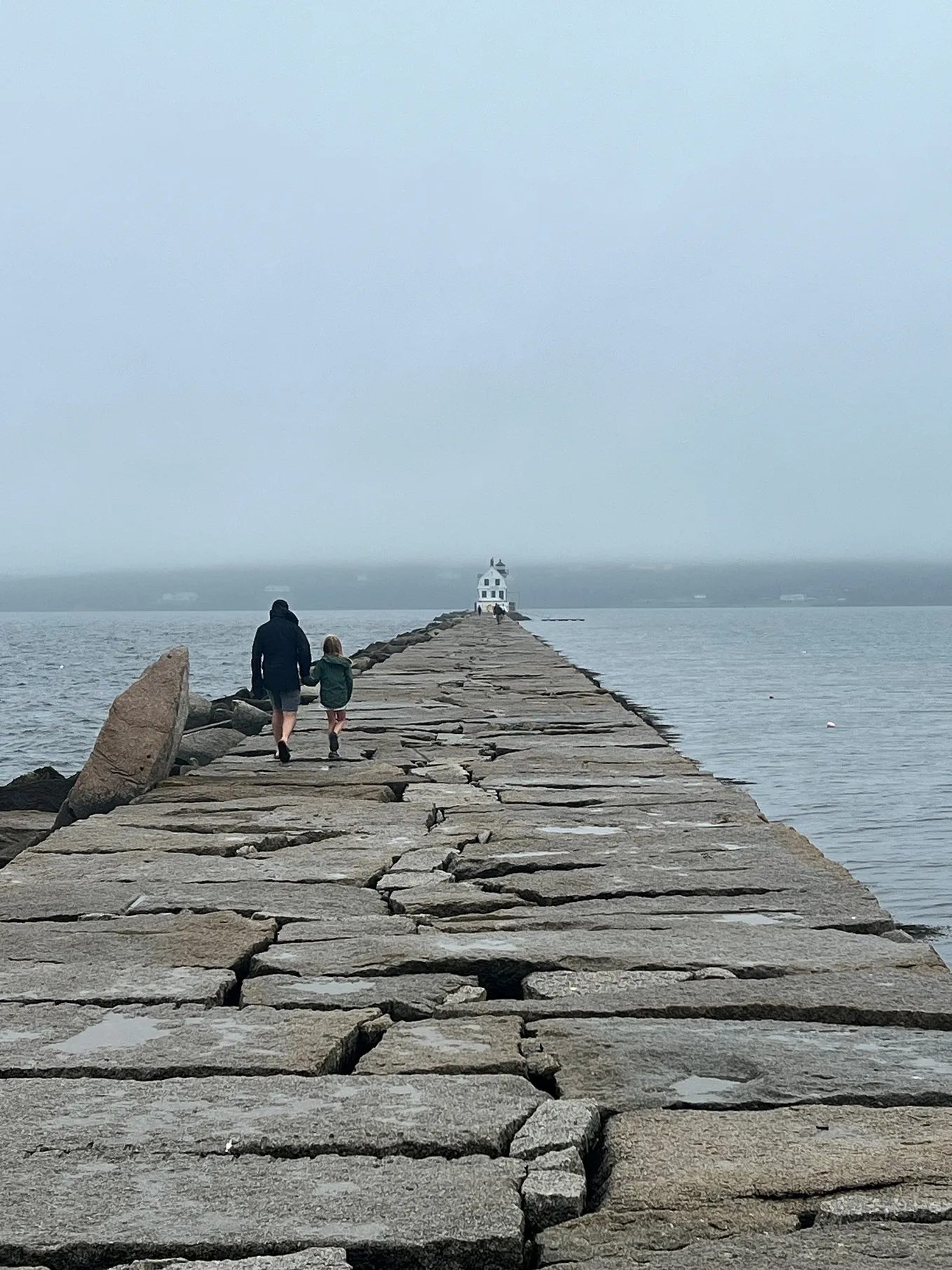 A man and his daughter hold hands and walk along a boardwalk in Maine.