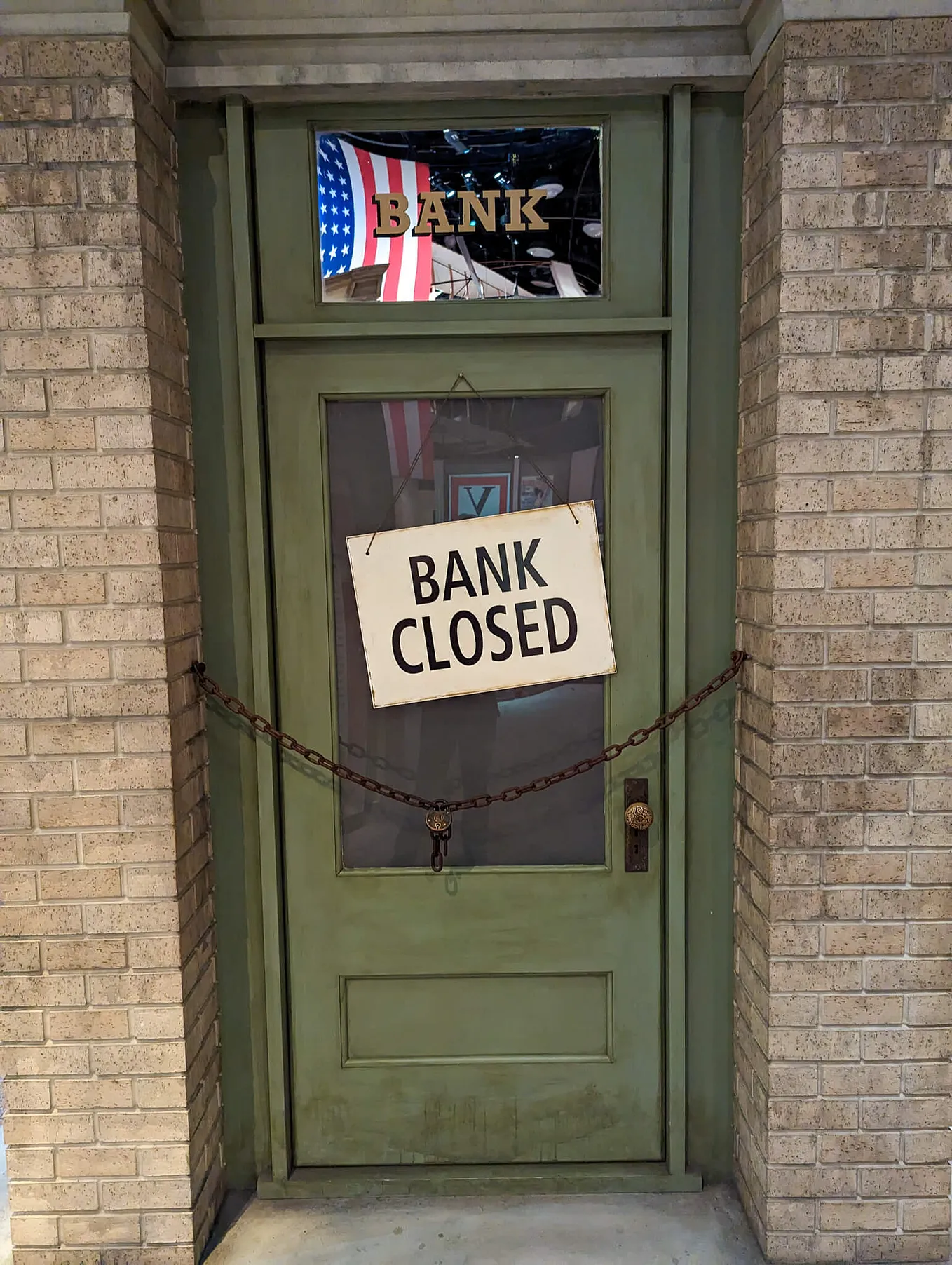 Faded green door with a sign reading “Bank Closed” and a chain hanging across the entry