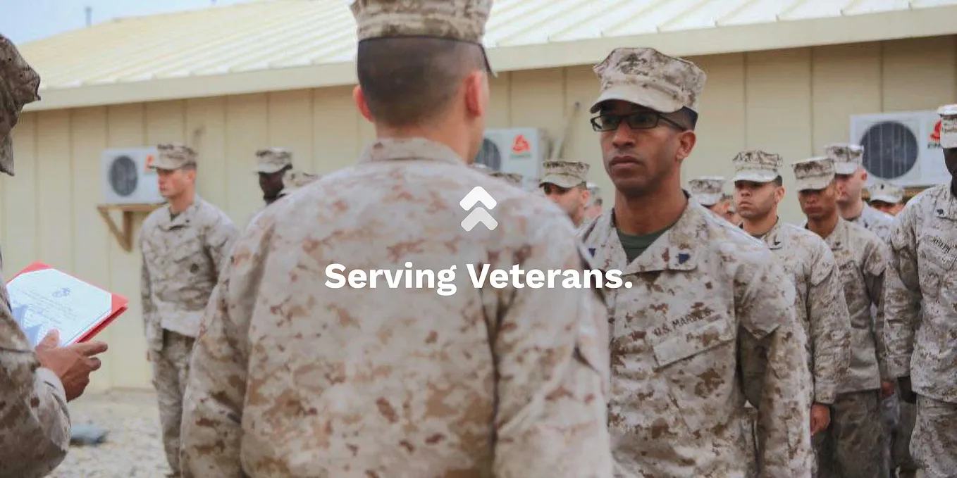 A group of marines in the background. In the foreground, one marine facing another with serious facial expressions.