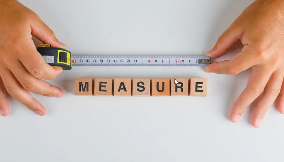 A photo of two hands holding a tape measure above a set of Scrabble tiles that spell out “Measure”.