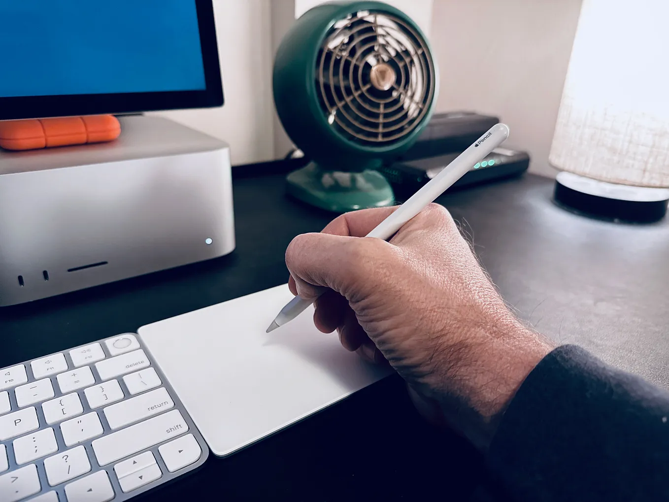 A hand holding an Apple Pencil over a Magic Trackpad