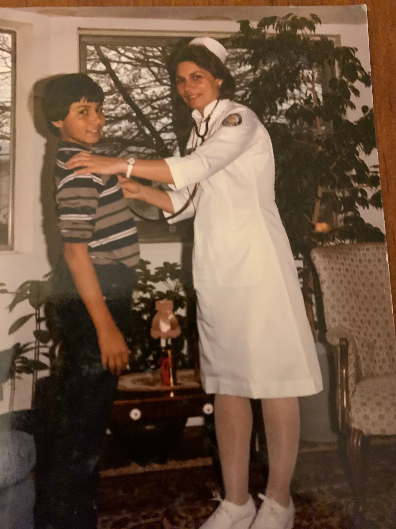 A nursing student, trying on her new white uniform and stethoscope on a young boy with a big smile.