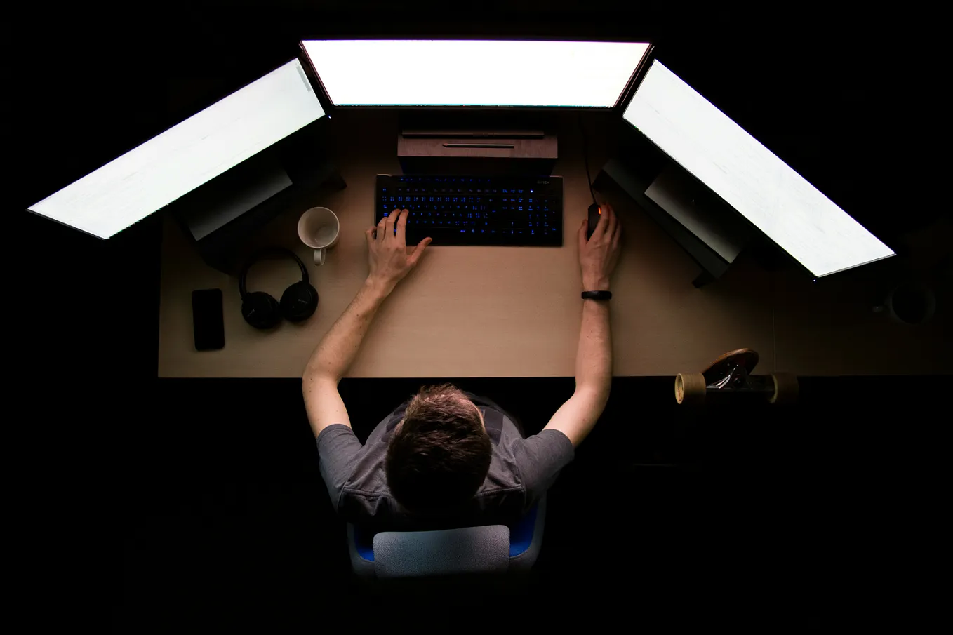 Man sitting at his desk in front of three computer monitors