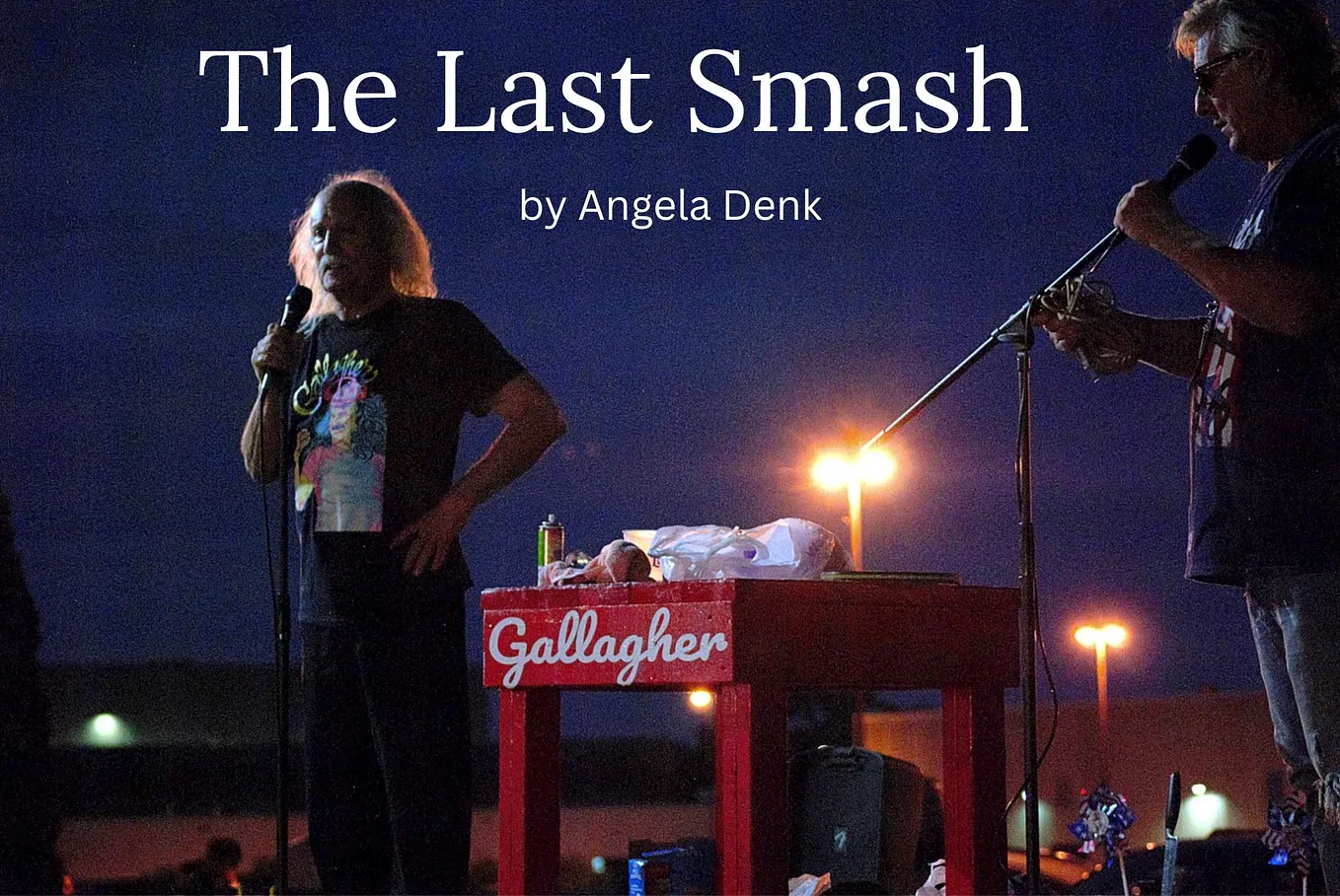 Late comedian Leo Gallagher standing on a stage at sunset next to a red table with white cursive letters reading “Gallagher” on it. On the right of the frame, songwriter Jimmi Zappas adjusts a microphone stand.