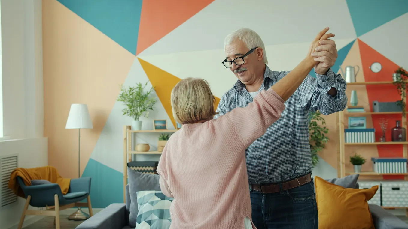 Older couple dancing together in a colorful living room, reflecting the emotional rewards and family connection often found in caregiving relationships. Photo by Vitaly Gariev on Unsplash