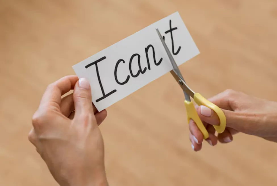 A photo of a person’s hands holding a small sign that says “I can’t” and using scissors to change it to “I can.”