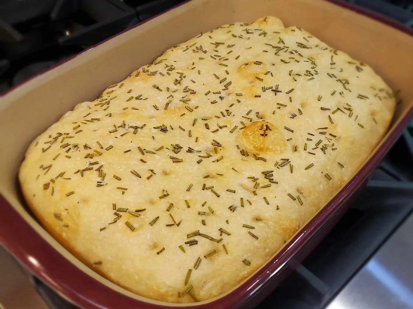 Image of baked focaccia, topped with sea salt and fresh rosemary, in stoneware pan