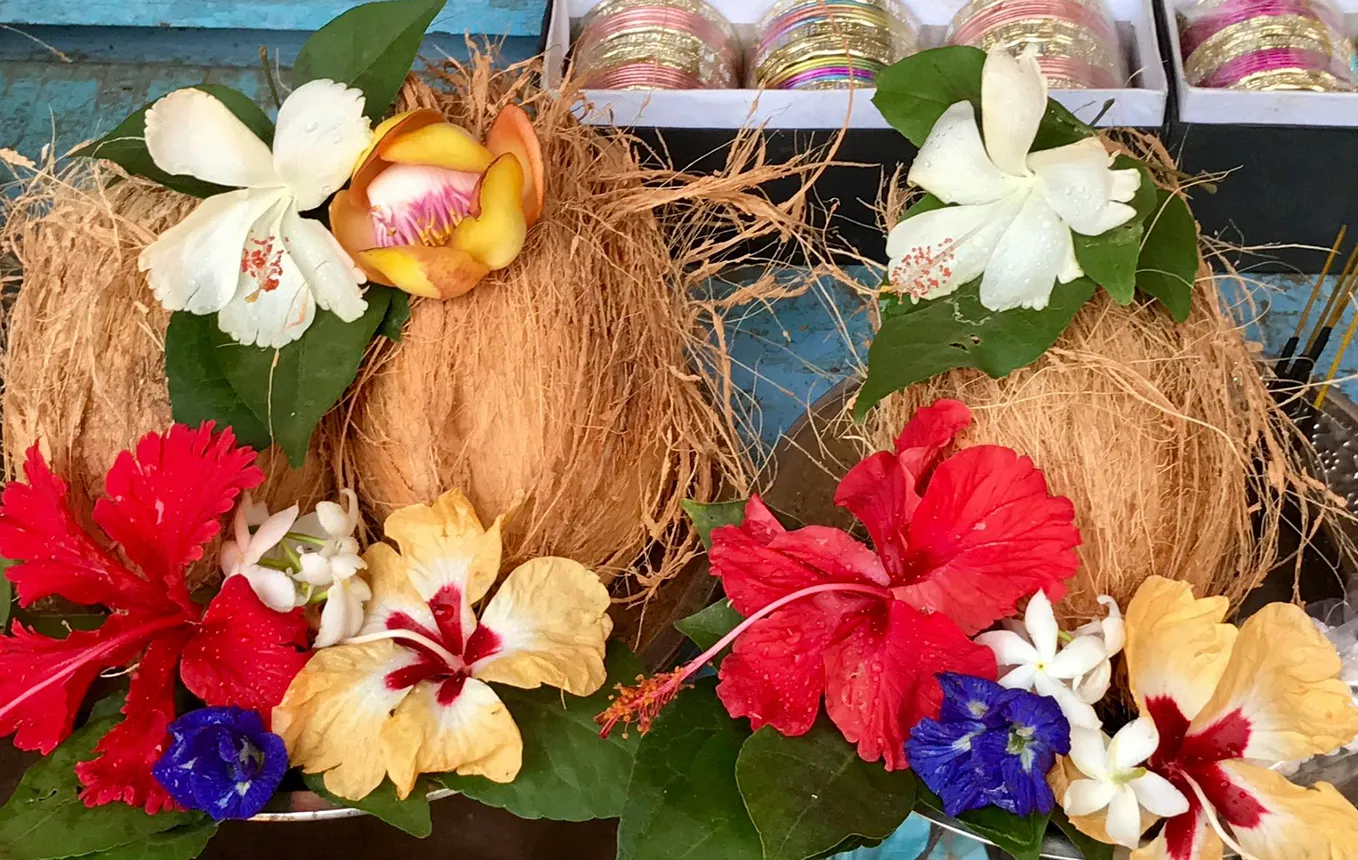 Author’s Image. A platter of offering to take to the deity with a coconut, hibiscus flowers of three colors, crepe jasmine, cannonball flowers, butterfly pea flowers.