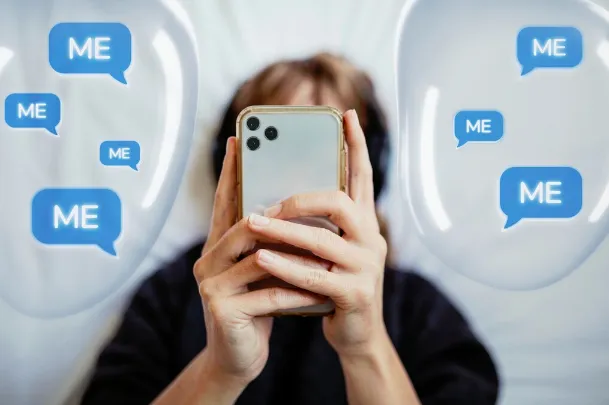 A photo of a person immersed in their phone with “Me” “Me” “Me” messages all around them.