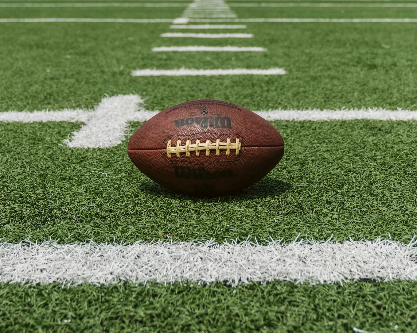 A photo of a football sitting on turf of a football field between the hash marks.