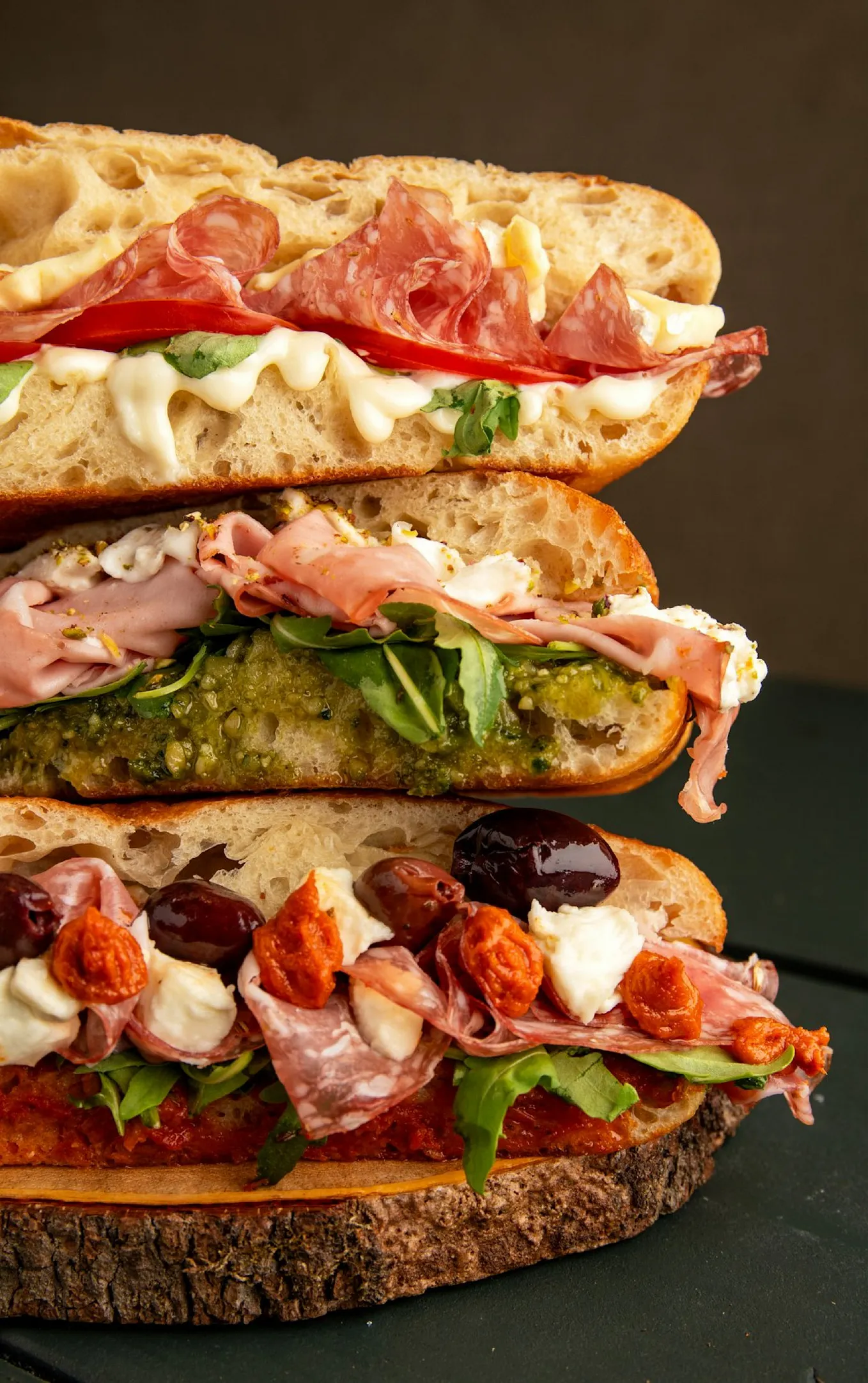 A selection of layered sandwiches with toppings including olives, burrata, arugula, prosciutto, sundried tomatoes and more.