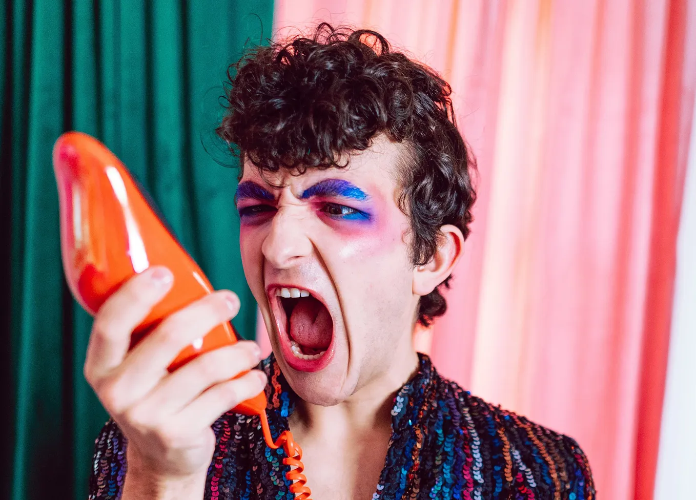 A flamboyant man yells at a telephone.