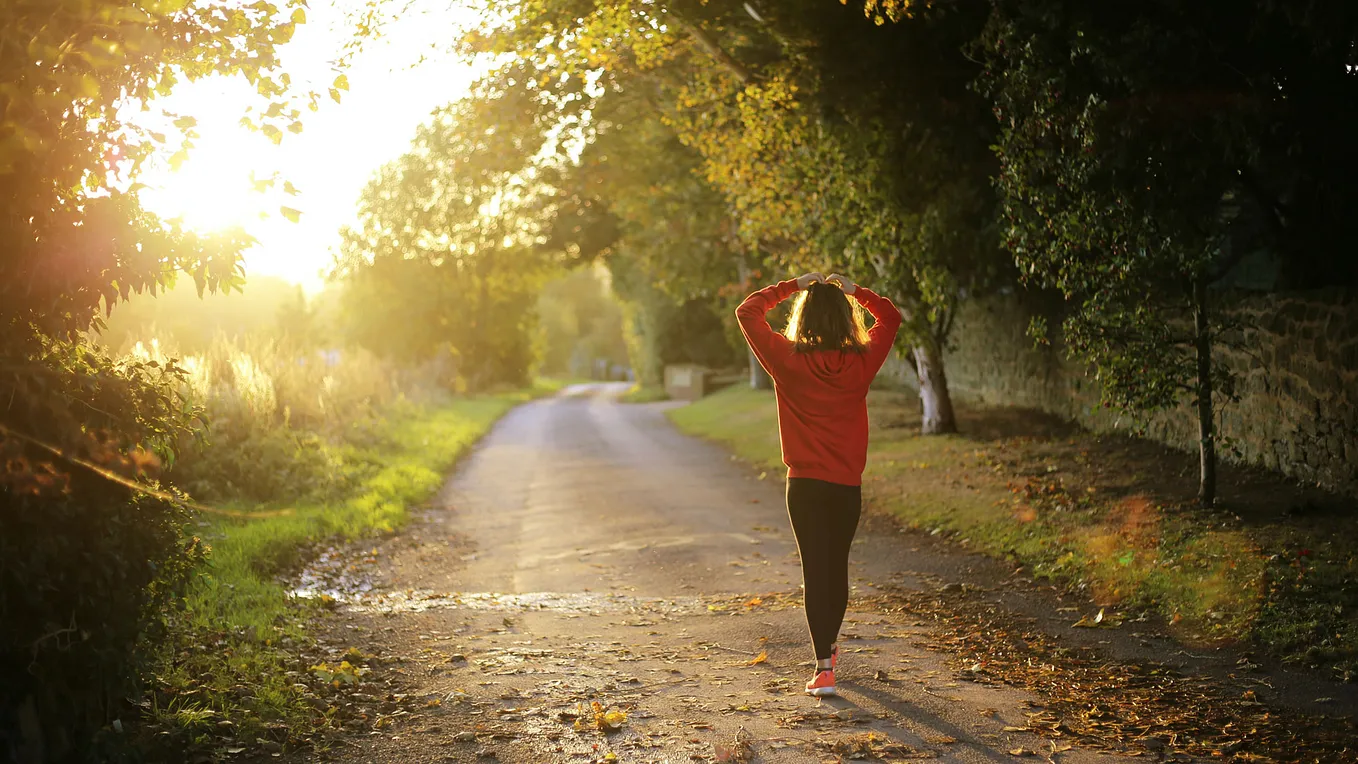 A woman going on an early morning run, hands above her head, breathless and enjoying the sunrise.