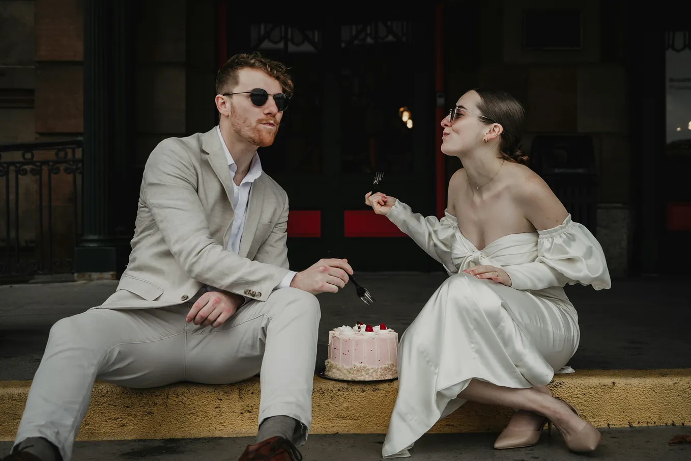 Couple sit on the stoop sharing a wedding cake