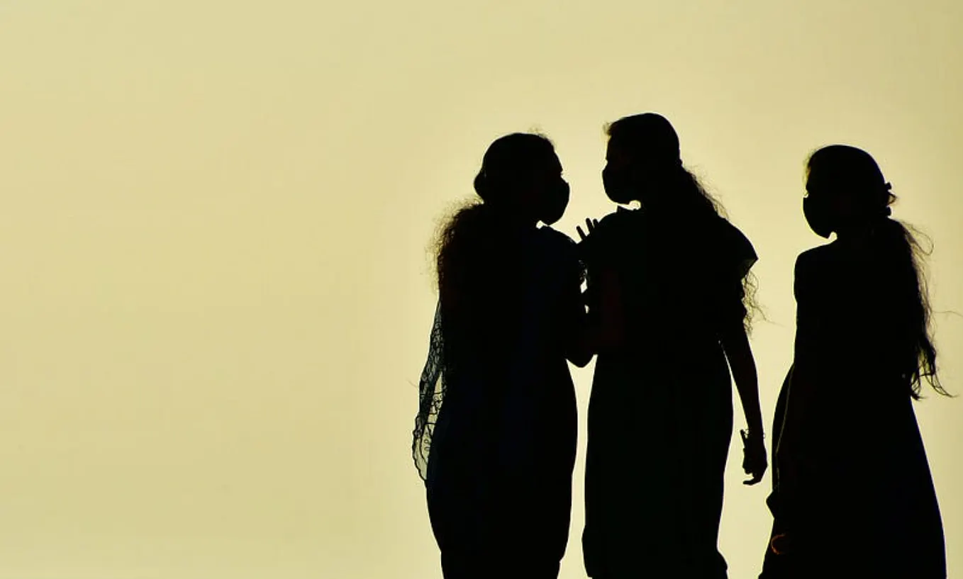Three women in silhouette, two of them holding hands with the 3rd slightly apart