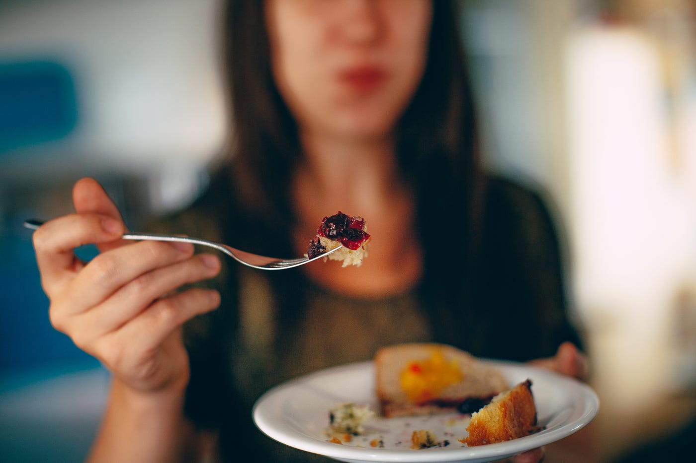 woman holding a plate with a full mouth offering a bite to the reader.