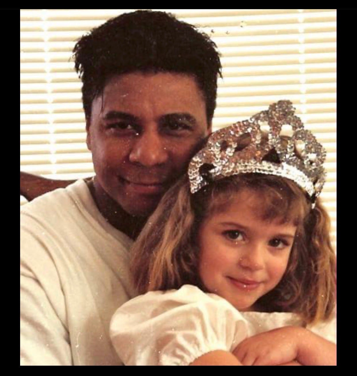 A Polaroid-looking portrait of a Black man with short hair hugging a child with shoulder-length hair and wearing a tiara.