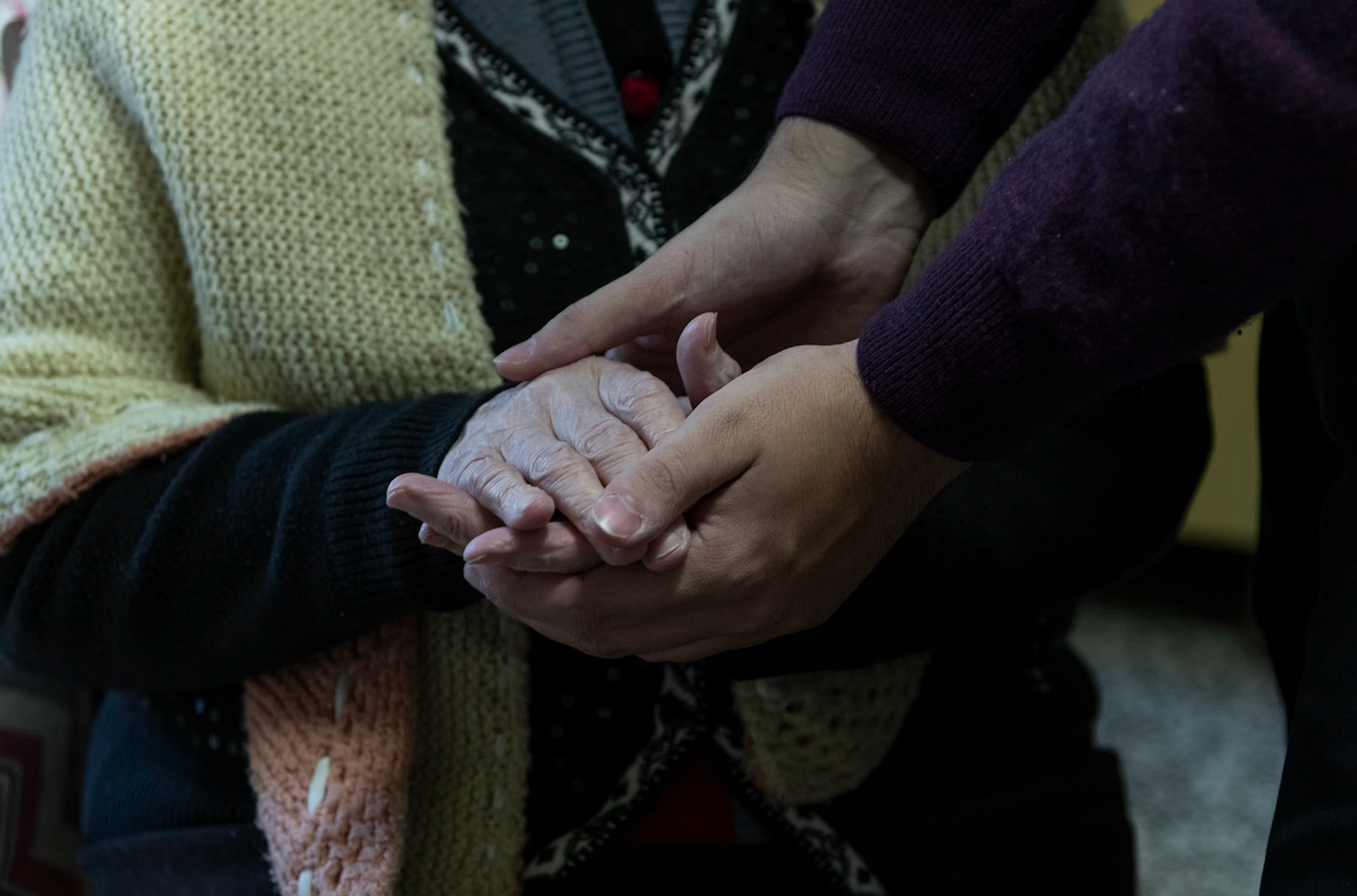 한 쌍의 손이 따뜻한 니트 카디건을 두른 노인의 손을 부드럽게 잡고 있습니다.<BR>