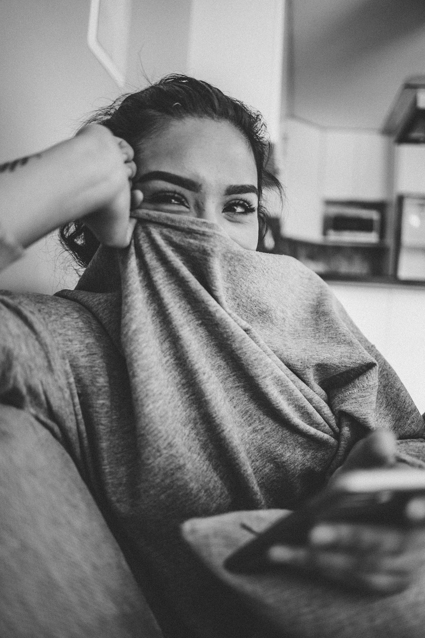 젊은 여성이 스웨트셔츠를 끌어올려 코와 입을 가리고 눈을 웃고 있습니다.<BR>