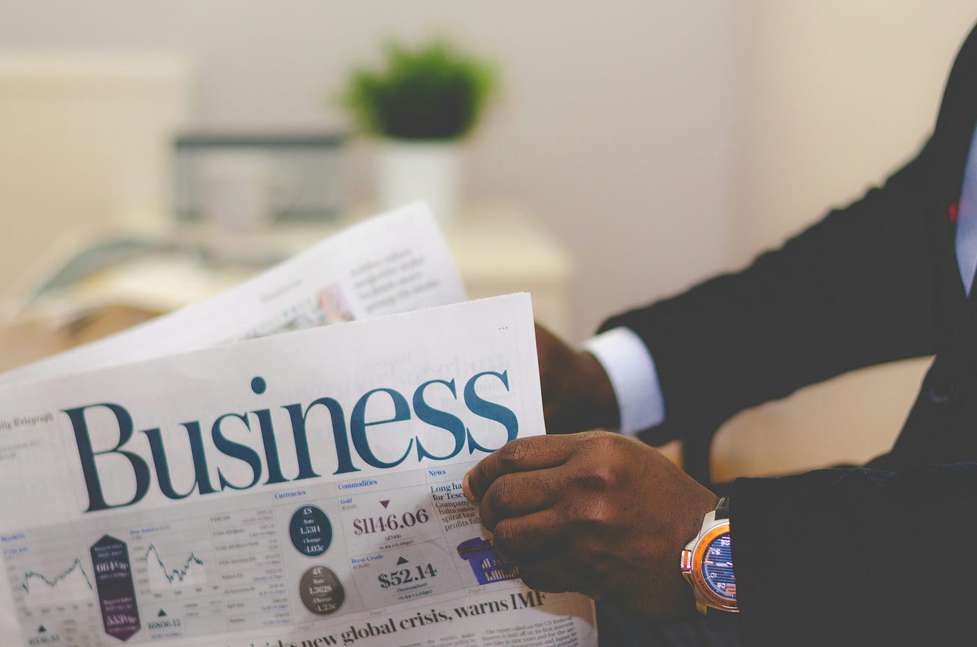 A person in a suit (with a nice wristwatch) reads a newspaper.